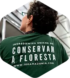 Mulher de cabelo escuro curto de costas, atrás de sua blusa está escrito "Ingredientes únicos conservam a floresta"